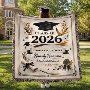 May include: A beige graduation blanket with a black mortarboard and the text "Class of 2026." The blanket features a scroll with a black ribbon, laurel wreaths, and the words "Congratulations" and "Namely Nameson."