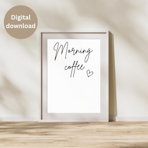 May include: A white framed print featuring the words "Morning coffee" in black script, with a small heart. A tan circle with "Digital download" is in the upper left corner. The print is on a wooden floor.