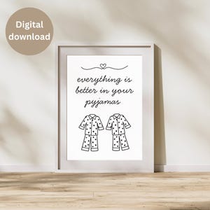 May include: A framed print with the text "everything is better in your pyjamas" above two pajama sets decorated with hearts. The print is in a white frame and is leaning against a wall. A digital download label is in the upper left corner.