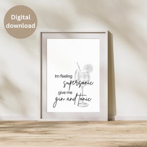 May include: A framed print with a white background features a line drawing of a gin and tonic cocktail. The text "I'm feeling supersonic give me gin and tonic" is written in a stylish font. A digital download label is in the upper left corner.