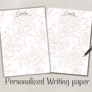 May include: Two sheets of personalized writing paper with the name "Emily" in elegant script. The paper features a floral and bird design in a soft pink hue. The bottom of the image reads "Personalized Writing paper". A black pen rests on the lined sheet.