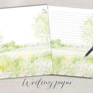 Puede incluir: Dos hojas de papel de escritura con un diseño de paisaje en acuarela. El diseño presenta un campo de flores silvestres, árboles y un pequeño pájaro. Una hoja está rayada y la otra en blanco. Un bolígrafo negro descansa sobre la hoja rayada. El texto "Writing paper" está en la parte inferior.