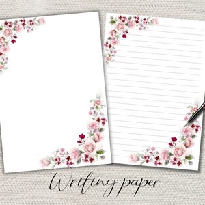 Op de afbeelding: Twee vellen wit schrijfpapier, één gelijnd en één blanco, versierd met aquarel bloemstukken in roze, bordeauxrood en groen. Een zwarte pen ligt op het gelijnde vel. De woorden "Writing paper" zijn cursief onderaan geschreven.