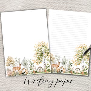 May include: Two sheets of white stationery featuring a watercolour forest scene at the bottom with a deer, foxes, and a hedgehog among trees. One sheet is blank, and the other has horizontal lines for writing. A black pen rests on the lined sheet.
