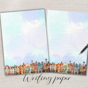 Könnte beinhalten: Zwei Blätter Schreibpapier mit einem Aquarelldesign. Der untere Teil des Papiers zeigt eine farbenfrohe Stadtlandschaft. Ein Blatt ist leer, das andere hat blaue Linien. Ein schwarzer Stift liegt auf dem linierten Blatt. Die Worte "Writing paper" sind kursiv geschrieben.