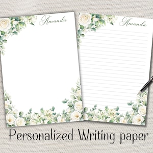 Peut inclure: Deux feuilles de papier à écrire blanc personnalisé avec le nom "Amanda" en écriture cursive. Le papier est décoré de roses blanches à l'aquarelle et de feuillage vert. Une feuille est lignée, et un stylo noir repose sur le côté. Le texte "Personalized Writing paper" est en bas.