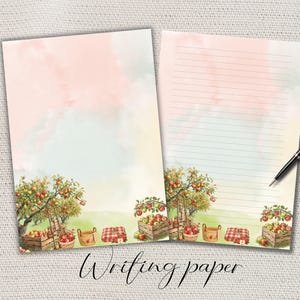 Può includere: Due fogli di carta da lettere con un'illustrazione ad acquerello di un frutteto di mele con alberi, cassette di legno piene di mele rosse, cesti di vimini e coperte a quadri rossi. Un foglio è bianco, l'altro presenta linee orizzontali.