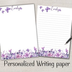 Könnte beinhalten: Zwei Blätter personalisiertes Briefpapier mit einem Blumen- und Schmetterlingsdesign in Lila- und Rosatönen. Der Name "Emily" steht oben. Ein Blatt ist liniert, das andere ist leer. Die Worte "Personalized Writing paper" stehen unten.