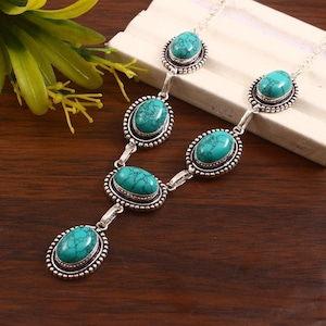 Puede incluir: Un collar plateado con piedras turquesas ovaladas. Cada piedra está engastada en un marco decorativo con un borde de cuentas. El collar tiene un diseño en forma de Y con múltiples piedras turquesas conectadas por eslabones plateados.