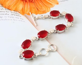 Peut inclure: Un bracelet en argent orné de pierres précieuses ovales rouge foncé. Le bracelet est composé de plusieurs pierres précieuses reliées par des maillons en argent, avec de petits motifs floraux entre certaines pierres. Le fermoir est un simple crochet et boucle.