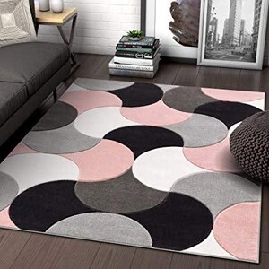May include: A patterned rug featuring a design of overlapping semi-circles in pink, black, grey, and white. The rug is placed on a wooden floor, adding a decorative element to the room.