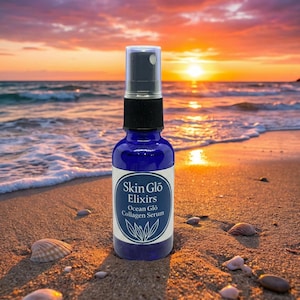 May include: A blue glass spray bottle of Skin Glo Elixirs Ocean Glo Collagen Serum on a sandy beach with seashells. The background features an ocean and a sunset with orange and yellow hues.
