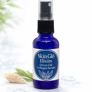 May include: A cobalt blue glass bottle of Skin Glo Elixirs Ocean Glo Collagen Serum. The bottle has a black spray nozzle and a white label with the product name and a botanical design. A seashell and leaves are in the background.