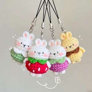 May include: Four crochet bunny charms with black eyes and blush cheeks. The bunnies are white with different colored outfits: green, red, purple, and yellow. Each charm has a silver clasp and black lanyard.