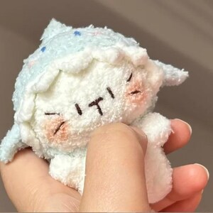 Peut inclure: Une peluche de mouton blanc avec un chapeau et des d&eacute;tails bleu clair. Le mouton a les yeux ferm&eacute;s, une petite bouche et des joues roses. Le jouet est tenu dans une main.