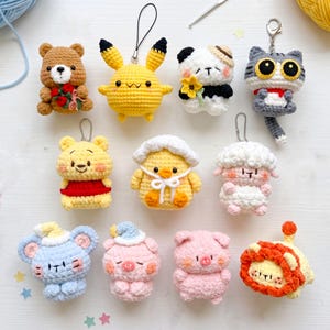 May include: A collection of ten small crocheted plush keychains featuring various characters including a brown bear with red flowers, a yellow creature, a panda, a gray cat, a yellow bear, a duck, a sheep, a blue mouse, and two pigs.