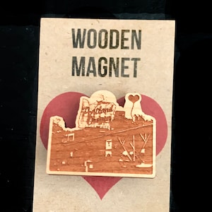 May include: Wooden magnet featuring a laser-engraved image of a building with the word "Oakland" on it. The magnet is shaped like a heart and has a small heart-shaped balloon above the building.
