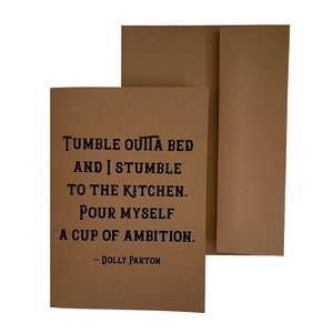 May include: A brown card with a quote from Dolly Parton that reads "Tumble outta bed and I stumble to the kitchen. Pour myself a cup of ambition."