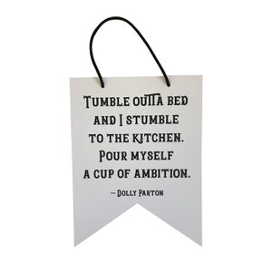 May include: White banner with black text that reads "Tumble ouita bed and I stumble to the kitchen. Pour myself a cup of ambition. - Dolly Parton"