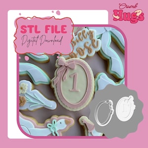May include: A collection of decorated cookies featuring a central oval cookie with a number one and a bow, alongside other shapes including a goose and flowers. The image includes text stating STL FILE Digital Download and Crumb Hugs.