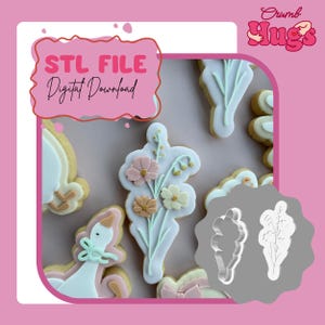 Pode incluir: Um arquivo STL para download digital de um cortador de biscoitos com design de buquê de flores. A imagem exibe biscoitos decorados com glacê azul claro, rosa e creme, ao lado de um formato de cortador de plástico branco em fundo rosa.