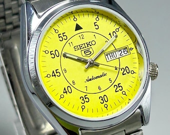 Reloj de pulsera para hombre Seiko 5 vintage reacondicionado, automático, esfera amarilla, 21 joyas, día, fecha, movimiento n.° 7S26A, fabricado en Japón, fondo transparente.