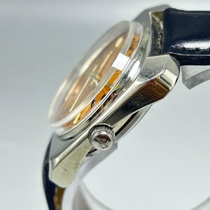 May include: A silver-toned wristwatch with a clear, domed crystal and a gold-toned face. The watch has a black leather band and a small, textured crown. The watch is angled, showing the side profile.