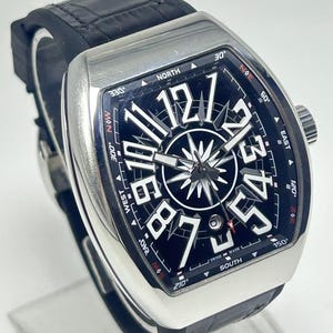 May include: A luxury wristwatch with a black face and silver case. The watch features large white numerals, a compass rose design, and a black leather strap. The watch face displays the text "SWISS MADE".