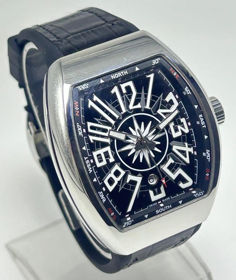 May include: A luxury wristwatch with a black face and silver case. The watch features large white numerals, a compass rose design, and a black leather strap. The watch face displays the text "SWISS MADE".