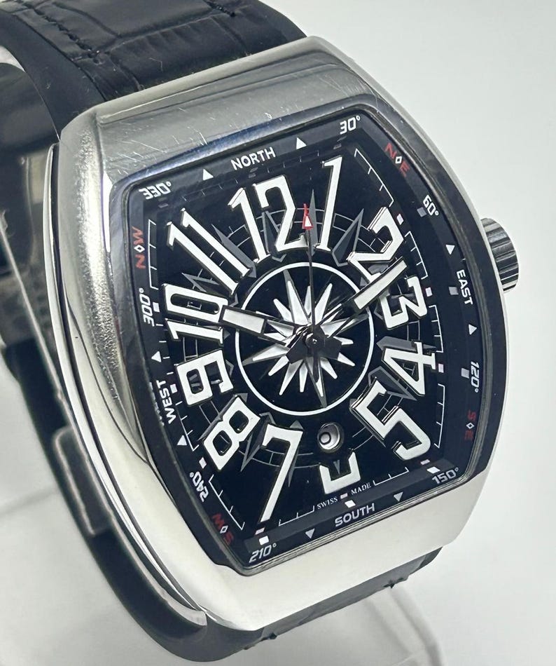 May include: A silver wristwatch with a black face, large white numerals, and a compass rose design. The watch has a black leather strap. The words "SWISS MADE" are visible.