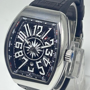 May include: A silver wristwatch with a black face and a black leather strap. The watch face displays large white numerals, a compass design, and the words "SWISS MADE". The watch has a rectangular case and a crown with a blue stone.