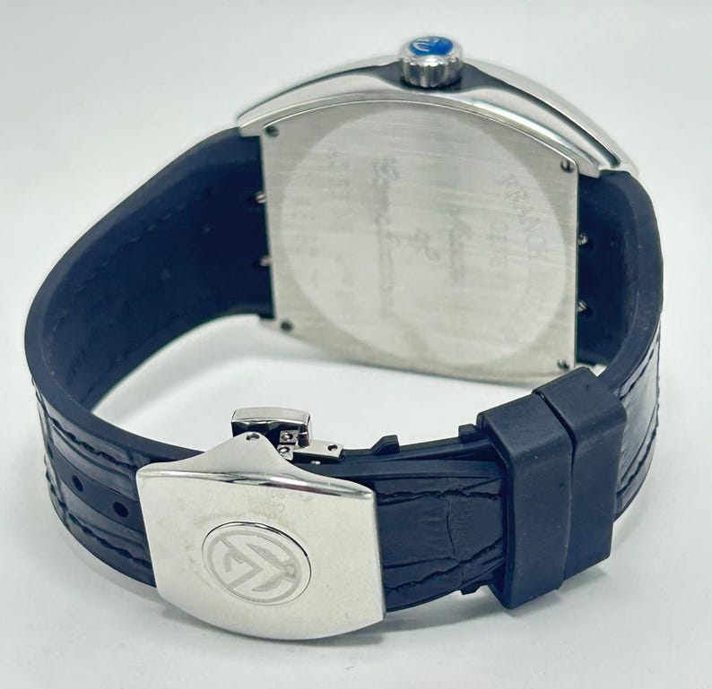 May include: A luxury wristwatch with a silver rectangular case and a dark blue leather strap. The watch has a silver clasp with a logo and a blue crown. The watch's back is silver with etched details.