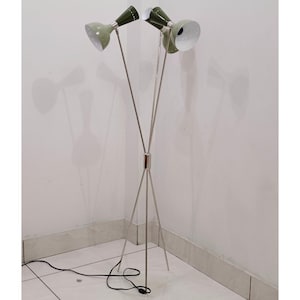 Op de afbeelding: Een moderne vloerlamp uit het midden van de eeuw met drie verstelbare lichtkoppen. De lamp heeft een statiefvoet en een zilverkleurig metalen frame. De lichtkoppen zijn olijfgroen met witte interieurs. De lamp is aangesloten op een stopcontact.
