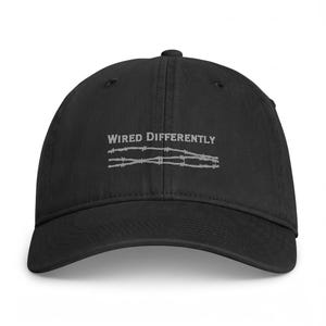 Peut inclure: Une casquette de baseball noire avec le texte brodé WIRED DIFFERENTLY en fil gris clair, placé au-dessus d'une illustration graphique de deux brins de fil barbelé également cousus dans une couleur gris clair assortie sur le panneau avant.