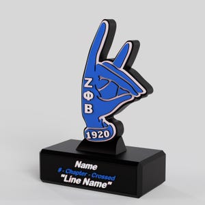 May include: A blue and black hand gesture sculpture with the letters Z, Φ, and B, and the number 1920. The sculpture is on a black base with text that reads "Name", "# - Chapter - Crossed", and "Line Name".