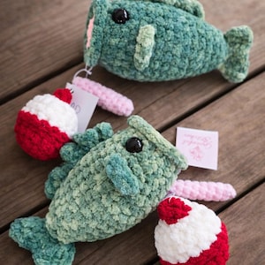 May include: Two handmade crochet fish toys in variegated green yarn with black plastic eyes. Each fish is attached to a small pink crocheted worm and a red and white round fishing bobber. A small white paper tag is attached to each toy.
