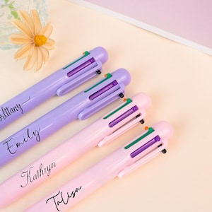 May include: Four multi-colour pens in shades of purple and pink are arranged diagonally. Each pen has a different name printed on it in black script: Brittany, Emily, Kathryn, and Talisa. The pens have green, purple, and orange accents.