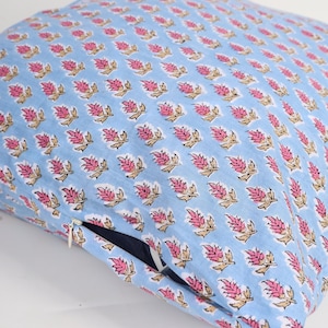 May include: A square cushion with a light blue background and a repeating pattern of pink and tan floral designs. The cushion has a hidden zip on one side. The cushion is on a white surface.
