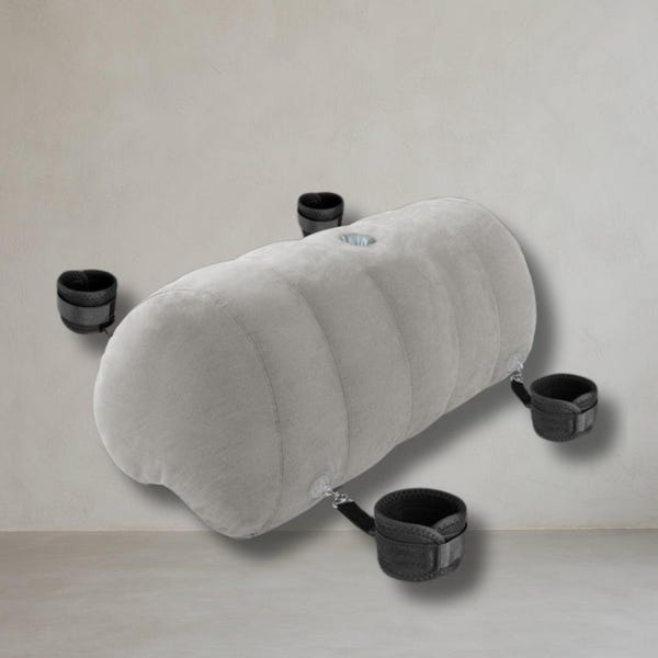 May include: A gray, elongated inflatable cushion with a series of vertical ridges. Four black wrist and ankle restraints are attached to the cushion. The background is a plain, light-colored wall.