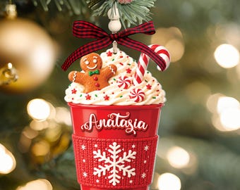 May include: A red Christmas ornament shaped like a coffee cup with a white snowflake pattern, a red and black plaid bow, and a gingerbread man topper. The cup features the name "Anatasia" in white script and the year "2026" printed in white.