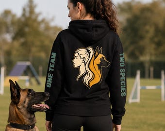 Könnte beinhalten: Ein schwarzer Kapuzenpullover mit einer Grafik auf der Rückseite, die das Profil einer Frau und das Profil eines Hundes zeigt, die in entgegengesetzte Richtungen blicken. Der Text ONE TEAM steht auf dem linken Ärmel und TWO SPECIES auf dem rechten.