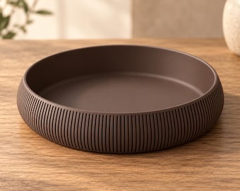 May include: A round, dark brown tray with a smooth, flat interior base and a low, vertical wall. The exterior side of the tray features a consistent, repeating pattern of thin, vertical grooves that wrap around the entire circumference.