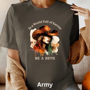 May include: Army green t-shirt featuring a watercolor illustration of a woman wearing a cowboy hat. The text "In a World Full of Karens, BE A BETH" is printed above and below the illustration. The word "Army" is printed at the bottom.