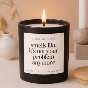 Könnte beinhalten: Eine brennende schwarze Kerze mit dem Text "smells like it's not your problem anymore" auf einem weißen Etikett. Die Kerze ist 130g und besteht aus 100% Sojawachs. Ein Holzdeckel liegt daneben.