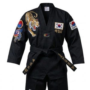 Puede incluir: Un uniforme de taekwondo negro que incluye una chaqueta con cuello en V, un tigre bordado en el pecho derecho, un parche con la bandera de Corea del Sur y un cinturón negro con el texto BLACK BELT y caracteres coreanos bordados en hilo dorado.