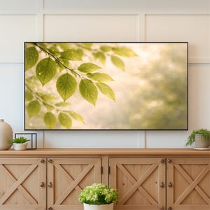 May include: A framed art print featuring a close-up of vibrant green leaves with water droplets, set against a soft, blurred background of light and shadow. The artwork is displayed above a wooden cabinet.