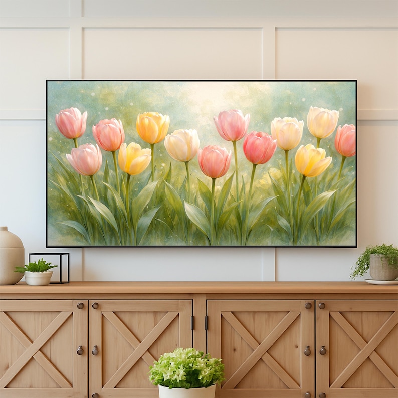 May include: A framed watercolor painting of tulips in shades of pink, yellow, and white. The flowers are set against a soft green and yellow background, with green leaves. The artwork is displayed above a wooden cabinet.
