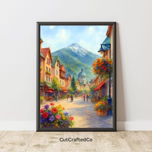 May include: Watercolor print of a European town square with a mountain backdrop. Buildings with red roofs and colorful flowers line the cobblestone street. The artwork is framed in a black border and features the text "CutCraftedCo".
