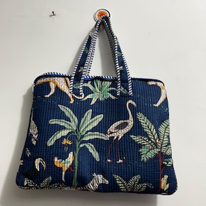 Könnte beinhalten: Eine gesteppte Stofftasche in Dunkelblau mit einem wiederkehrenden Muster aus tropischen Pflanzen, Palmen, Flamingos, Tukanen und Zebras. Die Tasche hat zwei Henkel mit blau-weiß gestreiftem Besatz und einen Reißverschluss an der Oberkante.