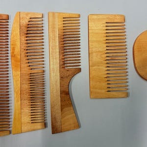 Könnte beinhalten: Eine Sammlung von fünf Holzkämmen in verschiedenen Formen und Größen. Die Kämme bestehen aus hellem und dunklem braunem Holz mit feinen Zähnen. Ein Kamm hat einen gebogenen Griff, ein anderer ist halbkreisförmig. Sie liegen auf einer hellgrauen Oberfläche.